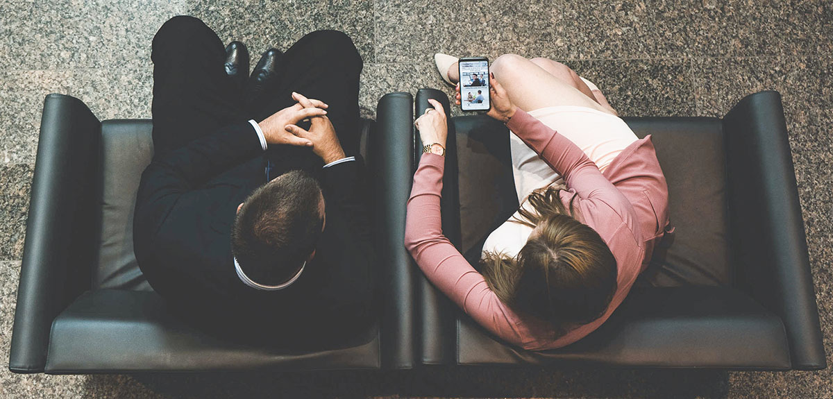 Two OIC employees sitting on chairs looking at a phone